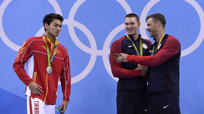 Peldēšanā ASV ir pārākas par Ķīnu, bet kopējā ieskaitē iet sīvi. Attēlā: olimpiskais čempions 100m peldējumā uz muguras Mērfijs (no labās) ar pārējiem medaļniekiem Plammeru un Sju