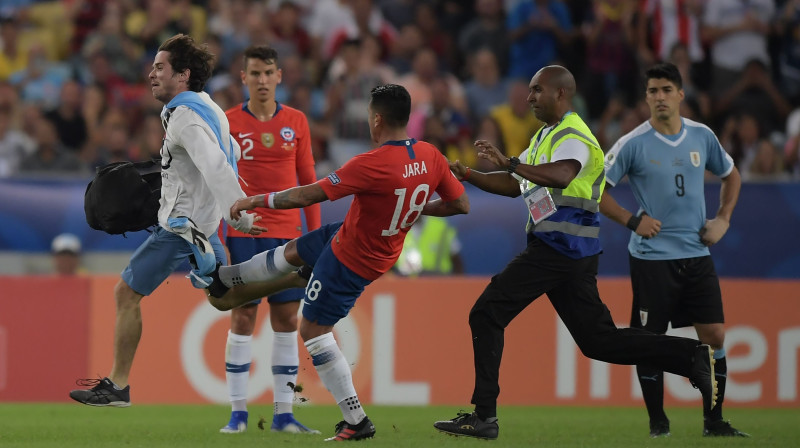 Čīles izlases futbolists Gonzalo Hara cenšas iespert pa laukumā izskrējušo līdzjutēju. Foto: AFP/Scanpix